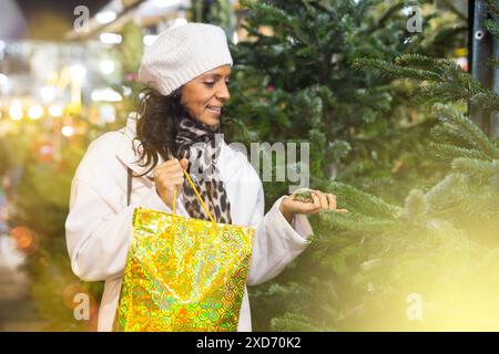 Femme hispanique gaie à la recherche d'un arbre de Noël sur un marché en plein air Banque D'Images