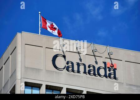 Ottawa, Canada - 15 juin 2024 : drapeau canadien et logo du gouvernement canadien à l'édifice du MDN sur la promenade Colonel By à Ottawa Banque D'Images