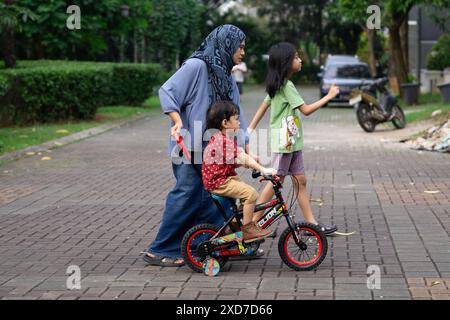 Enfant apprenant à faire du vélo avec l'aide de sa mère à l'extérieur dans Residential Street Banque D'Images