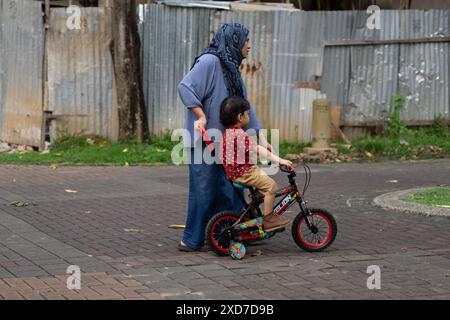 Enfant apprenant à faire du vélo avec l'aide de sa mère à l'extérieur dans Residential Street Banque D'Images