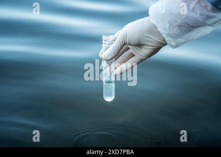 examen de la qualité de l'eau dans un réservoir naturel. un tube à essai dans la main d'un homme avec de l'eau pour vérifier sa pureté. Banque D'Images