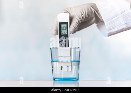 Testeur de compteur de qualité de l'eau immergé dans le verre à boire, sur fond bleu. Mesure des impuretés nocives, eau distillée, eau purifiante pour la santé Banque D'Images