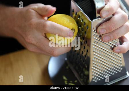 Un homme blanc râpant du zeste de citron avec une râpe. Préparation des aliments. Ingrédients rafraîchissants pour la cuisson et la cuisson. Gros plan sur l'image couleur du citron. Banque D'Images