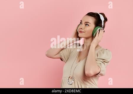 Jeune femme enceinte dans une robe écoutant joyeusement des écouteurs sur un fond rose. Banque D'Images