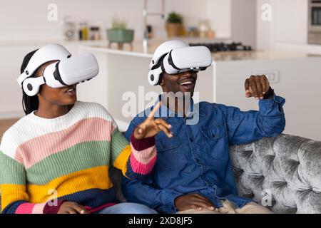 Porter des casques VR, jeune couple profitant de l'expérience de réalité virtuelle sur le canapé Banque D'Images
