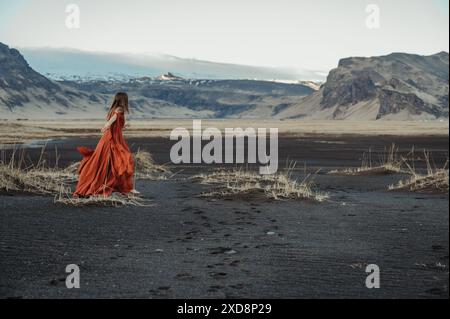 Femme en robe rouge marchant dans le paysage islandais sauvage Banque D'Images