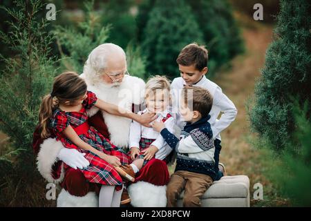 Père Noël avec quatre enfants en tenue festive à une ferme d'arbre de Noël, Banque D'Images