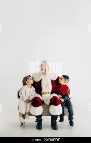 Père Noël avec deux enfants assis sur un canapé, l'un portant un o blanc Banque D'Images