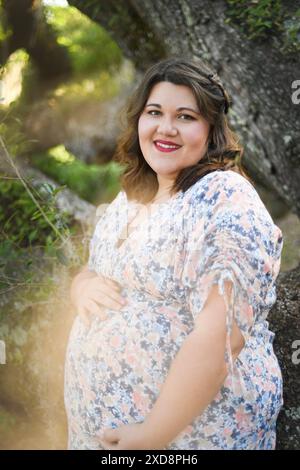 Femme enceinte souriante dans une robe florale, debout à l'extérieur avec l'esprit Banque D'Images