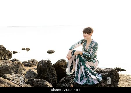 Une femme dans une robe à motifs assise sur des rochers au bord de l'eau, smil Banque D'Images