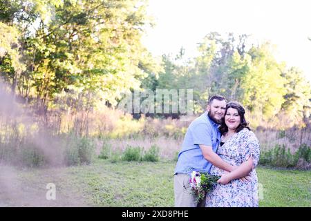 Heureux couple enceinte embrassant dans une prairie verte ensoleillée, holdin Banque D'Images