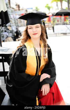 Diplômée en casquette et robe, assise à l'extérieur, paraissant fière Banque D'Images