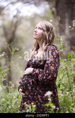 Femme enceinte dans une robe florale debout dans un bois serein, Banque D'Images