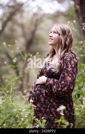 Femme enceinte souriante dans une robe florale debout dans un WO serein Banque D'Images