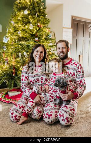 La famille est assise devant le sapin de Noël portant un pyjama de vacances Banque D'Images