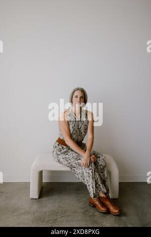Femme aux cheveux gris assise sur un banc contre un mur blanc Banque D'Images