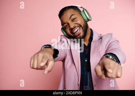 Jeune homme afro-américain en accolades pointe vers la caméra tout en portant des écouteurs sur un fond rose vif. Banque D'Images