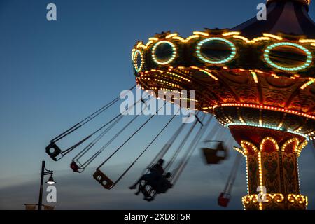 Balade en carrousel illuminée en mouvement au crépuscule. Banque D'Images