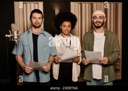 Trois personnes se tiennent debout dans un studio d'enregistrement tenant des feuilles de paroles, se préparant pour une séance de répétition de groupe de musique. Banque D'Images