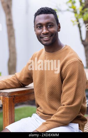 Homme en vêtements décontractés assis à la table en bois, souriant à la caméra Banque D'Images