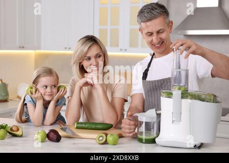 Famille heureuse avec presse-agrumes et produits frais faisant boisson à la table en marbre blanc dans la cuisine Banque D'Images