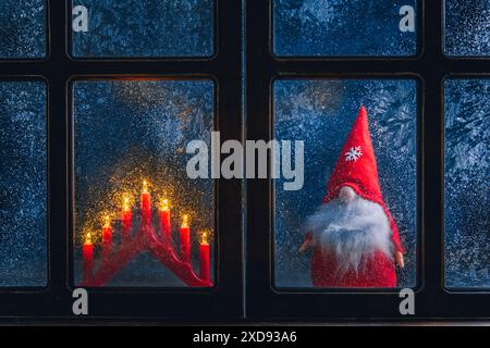 Noël, nouvel an, composition d'hiver. Gnome de Noël et bougies derrière une fenêtre gelée à motifs givré Banque D'Images