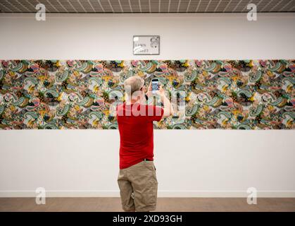 Un homme dans un tshirt rouge se tient devant une longue œuvre rectangulaire représentant Paisley Pattern prenant une photo avec son téléphone portable Banque D'Images