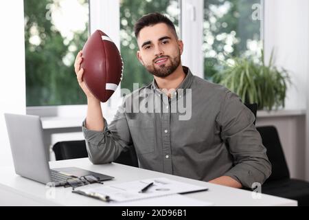 Jeune homme avec ballon de football américain à table dans le bureau Banque D'Images