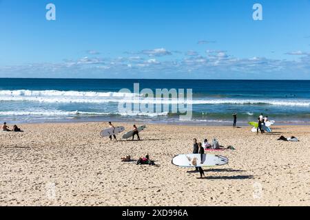 Manly Beach à Sydney, occupé avec des surfeurs sur la plage transportant des planches de surf, ciel bleu hiver jour, Sydney Northern Beaches, NSW, Australie, 2024 Banque D'Images