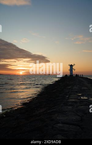 Moulin à vent à l'ancienne sur la jetée rocheuse sur la côte de l'île d'usedom le long de la mer baltique de Pologne avec beau coucher de soleil romantique et spectaculaire Banque D'Images