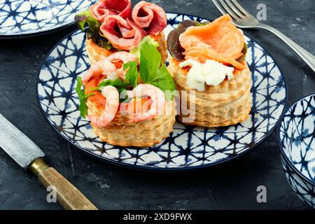 Tartelettes de pâte feuilletée avec du poisson, des crevettes et du bacon sur une assiette sur la table. Banque D'Images