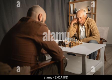 Père et fils jouant aux échecs à la maison assis dans le salon le soir. Vie de retraite Banque D'Images