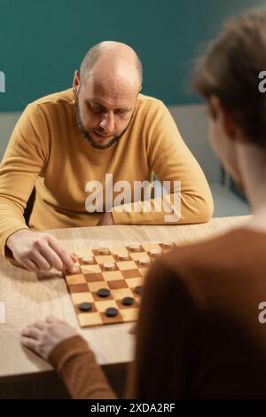 Amis jouant aux échecs assis à table à la maison dans une atmosphère chaleureuse, hipster avec un ami jouant au jeu de société. Passe-temps et loisirs Banque D'Images