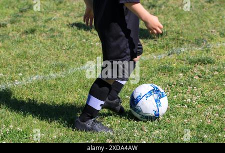 Gros plan d'un jeune joueur de football qui court avec le ballon portant un uniforme noir sur un terrain en herbe. Banque D'Images