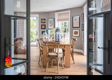 Vue à travers la double porte à la table Conran en bois avec des chaises d'OKA dans la rénovation de maison de campagne du 16ème siècle, Suffolk, Angleterre, Royaume-Uni Banque D'Images