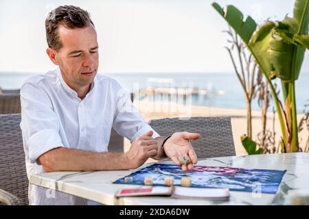Portrait de l'homme qui roule des dés dans l'ancien jeu de conseil indien Leela, assis sur le bord de la mer Turquie, Alanya - 14 avril 2024 Banque D'Images