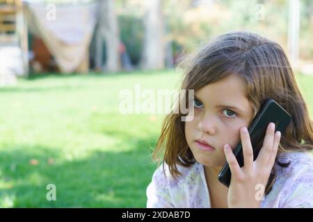 Gros plan d'une jeune fille de neuf ans parlant sur son smartphone dans le parc Banque D'Images