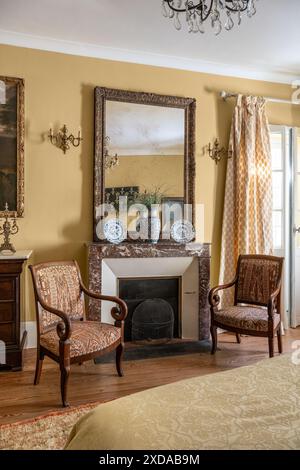 Paire de fauteuils rembourrés au coin du feu dans une chambre jaune dans un hôtel particulier en pierre rénové datant de 1770 à Saulieu, Bourgogne, France. Banque D'Images