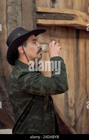 latino Man renifle parfum de vin dans une cave avec un tonneau en bois à l'arrière-plan dans une tournée à Cafayate, Argentine Banque D'Images