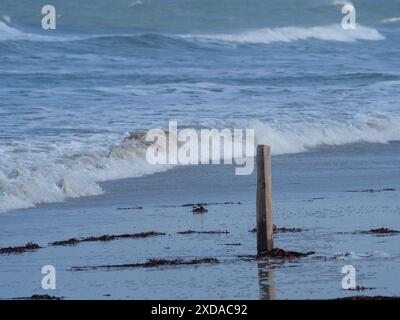 Un seul poteau en bois se dresse dans l'eau peu profonde sur la plage tandis que les vagues roulent sur le rivage, jaillissent. basse-saxe, mer du nord, allemagne Banque D'Images