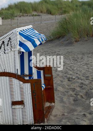 Une chaise de plage blanche avec des rayures bleues se dresse sur une plage de sable en face d'un paysage de dunes, juist, frise orientale, allemagne Banque D'Images