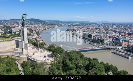 Budapest, Hongrie. 21 juin 2024 : Panorama de la capitale hongroise et statue de la liberté sur la Citadelle de Gellért Hill, érigée en 1947 en souvenir de la libération soviétique de la ville pendant la seconde Guerre mondiale. Aujourd'hui, les Hongrois commémorent le 80e anniversaire d'un réseau unique dans l'histoire de l'Holocauste en Europe: les maisons de l'étoile jaune, une partie des «lois juives». Du 21 juin 1944 jusqu'à la création du ghetto, 220 000 Juifs ciblés ont été obligés de vivre dans des bâtiments désignés après avoir été expulsés de leurs maisons. Comme le ghetto, les maisons ont servi de phase préparatoire à la déportation. Crédit : Kevin Izorce/Alamy Live News Banque D'Images