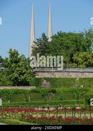 Deux clochers pointus s'élèvent au-dessus d'un jardin bien entretenu avec des fleurs colorées et de hautes haies, wuerzburg, bavière, allemagne Banque D'Images