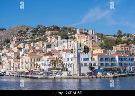 Une ville portuaire pittoresque avec des bâtiments de plusieurs étages sur la côte, nichée dans un paysage montagneux sous un ciel bleu clair, Symi Island Banque D'Images