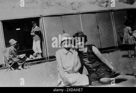 Deux dames, (décrites comme Win et Alice) assis sur une plage avec des cabanes de plage et d'autres personnes en arrière-plan. Mode et culture. Tiré d'une collection de photographies instantanées d'un groupe de femmes, 1928. Il y avait peu d'annotations sur les photos, mais les femmes semblaient voyager en groupe et avaient clairement un goût pour le comté anglais de Kent. Quelques-unes des photos suggèrent qu'elles ont pu être féministes de leur époque et, bien qu'elles soient largement inconnues, je les ai incluses car elles représentent certaines des modes de l'époque. Banque D'Images