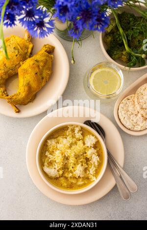 Ragoût de lapin avec du riz, du brocoli et des gâteaux de riz, une table servie avec de la nourriture et un vase de fleurs, un délicieux déjeuner copieux ou dîner Banque D'Images