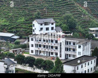 Shexian. 21 juin 2024. Une photo prise par un drone aérien le 21 juin 2024 montre un hélicoptère livrant des fournitures sur le toit d'une école primaire dans le canton de Shaolian dans le comté de Shexian, dans la province d'Anhui, à l'est de la Chine. Les pluies continues ont touché de nombreuses régions de l'est et du sud de la Chine, faisant des victimes, endommageant les récoltes et coupant les routes. Les autorités locales ont relevé les niveaux d'intervention d'urgence afin de minimiser l'impact des conditions météorologiques extrêmes. Crédit : Fan Chengzhu/Xinhua/Alamy Live News Banque D'Images