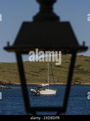 Un voilier ancré dans les eaux bleues claires près du phare de Faro de Favaritx, Minorque. Le littoral accidenté et le ciel spectaculaire offrent un arrière-plan magnifique Banque D'Images