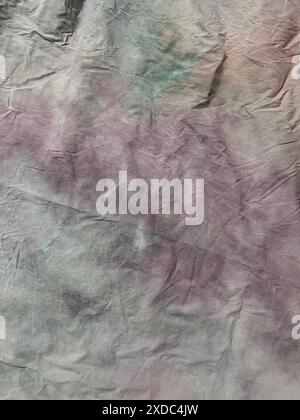 Cette image montre un motif aquarelle abstrait sur un morceau froissé de tissu gris. Le motif est un mélange de tons violet et vert délavés, créant un U. Banque D'Images