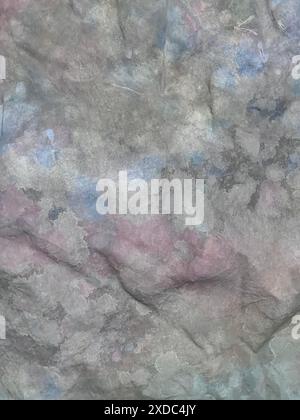 Une image en gros plan d'une surface rocheuse rugueuse et grise avec de subtiles taches bleues et roses. La roche a une texture naturelle avec de petites fissures et crevasses. L'image Banque D'Images